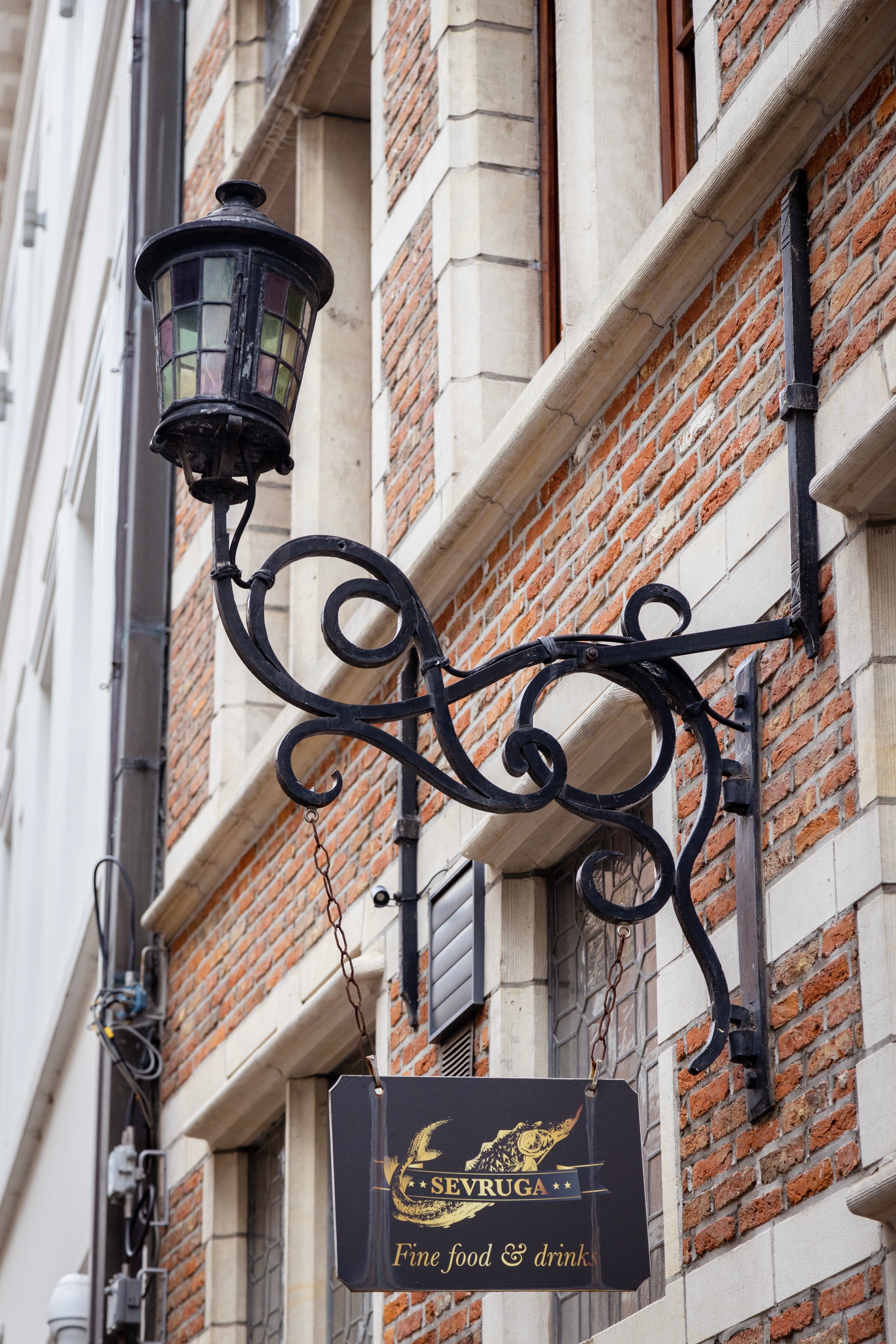 An iron street lamp with stained glass hangs from a brick wall on an old street — Antwerp City, Belgium