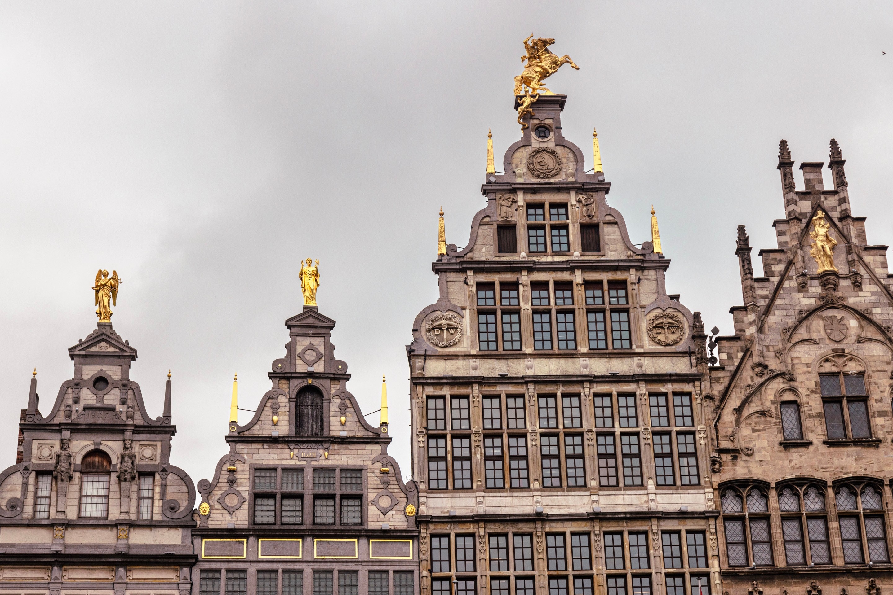 Four mediaeval mechant storefronts that surround the Market Square. It is decorated with golden statues; obelisks, priests, angels and a large statue of St George slaying the dragon — Antwerp City, Belgium