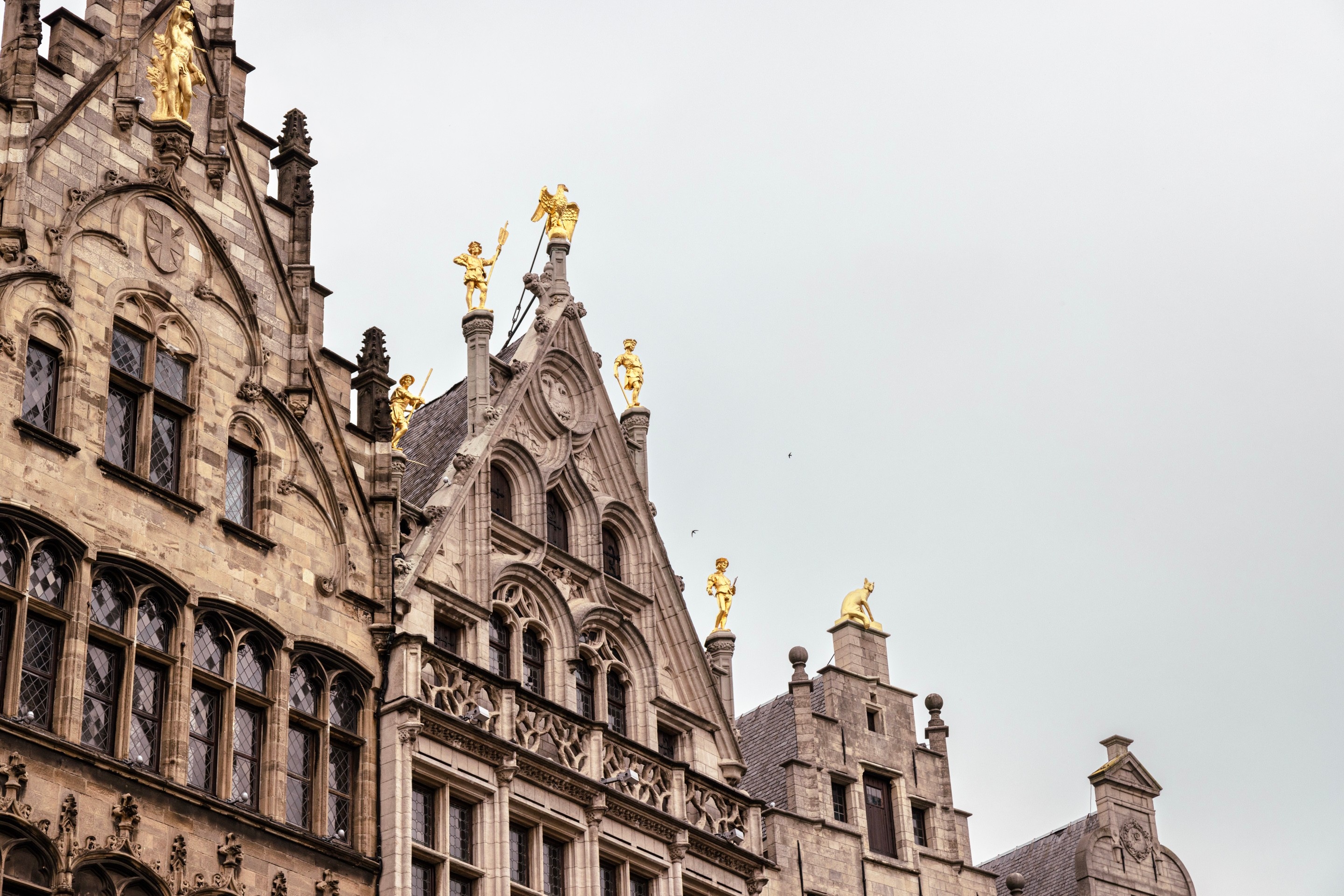 Four mediaeval mechant storefronts that surround the Market Square. It is decorated with golden statues; obelisks, priests and a large statue of St George slaying the dragon — Antwerp City, Belgium