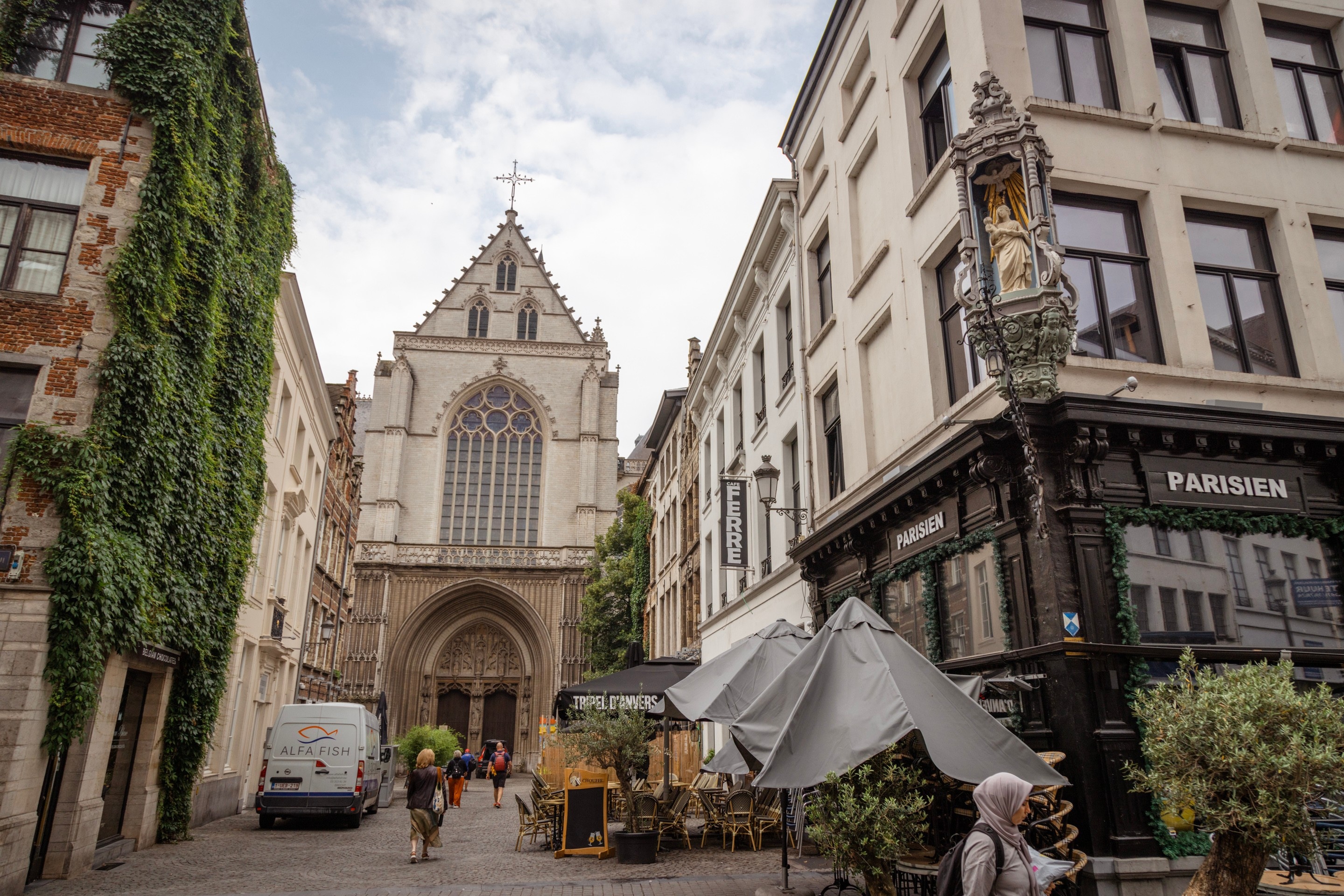 A street scene in the center of Antwerp City, with a churc and ivy covering a building to the left. On the corner above a restaurant hangs a "Corner Mary" — a religious shrine that adorns many of corners of the buildings on the streets of the city — Belgium