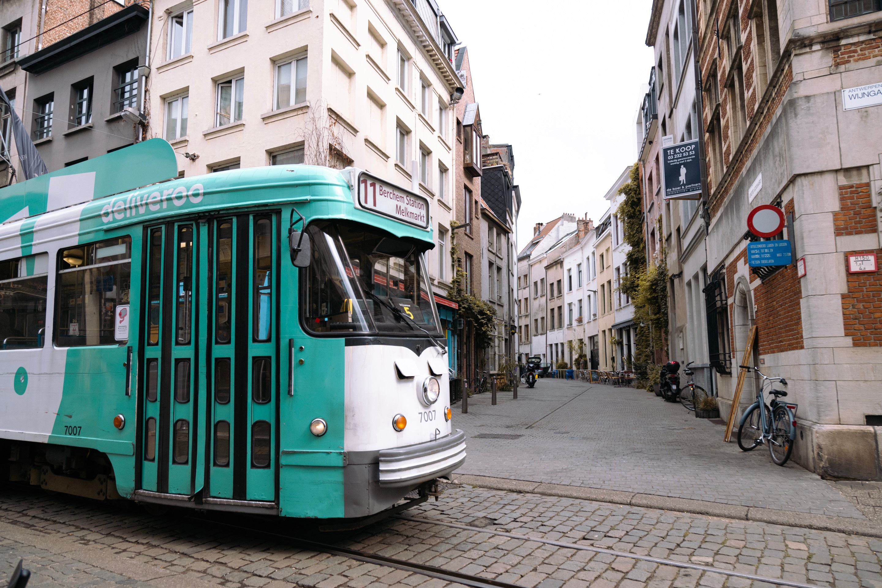 A pastel green painted tram travels along a cobbled street — Antwerp City, Belgium
