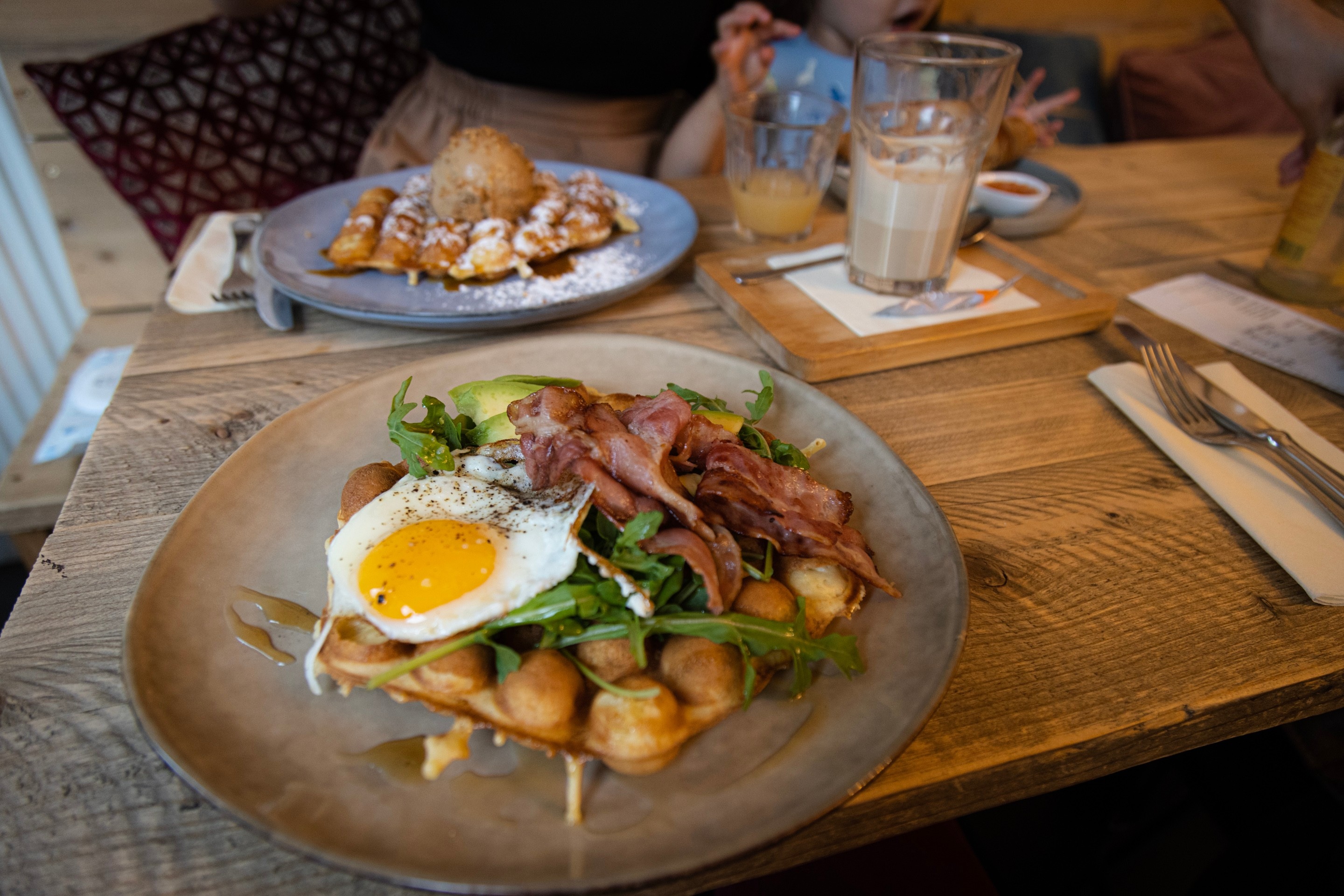 A tasty looking dish of Belgian waffles topped with bacon, eggs and avocado — placed upon a wooden table — Antwerp City, Belgium