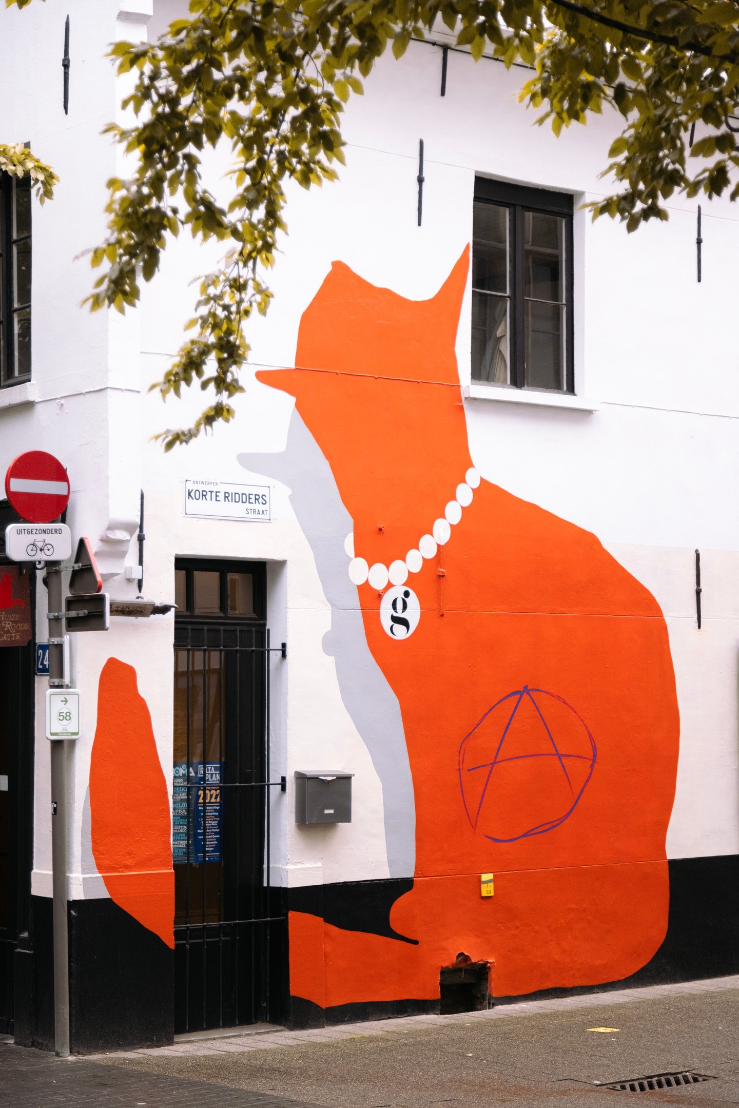 A large red silhouette of a cat wearing a pearl necklace decorates the side of a shop building — Antwerp City, Belgium