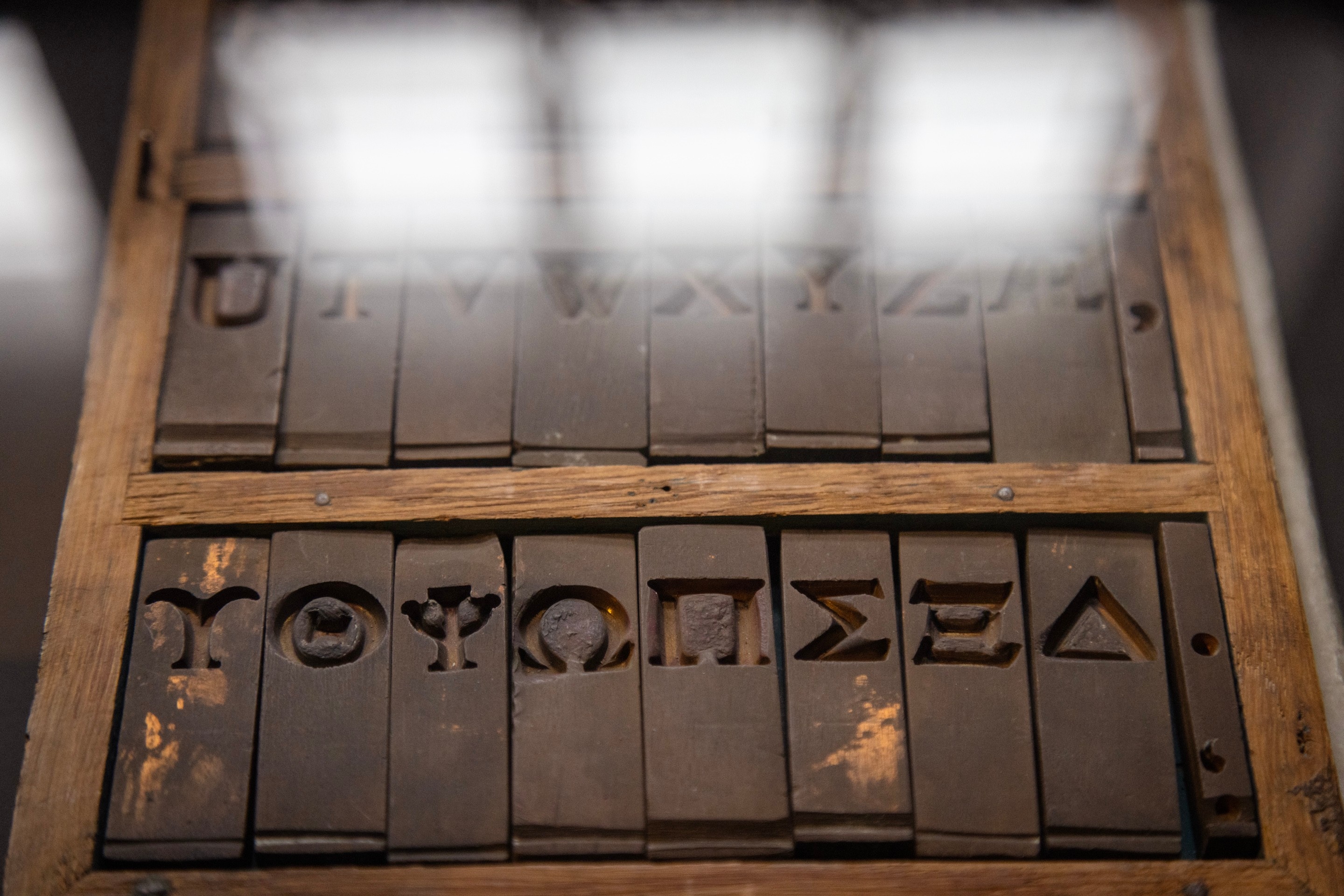 A case of special Greek letter moveable type covered in glass reflecting the windows behind — Museum Plantin-Moretus, Antwerp, Belgium 
