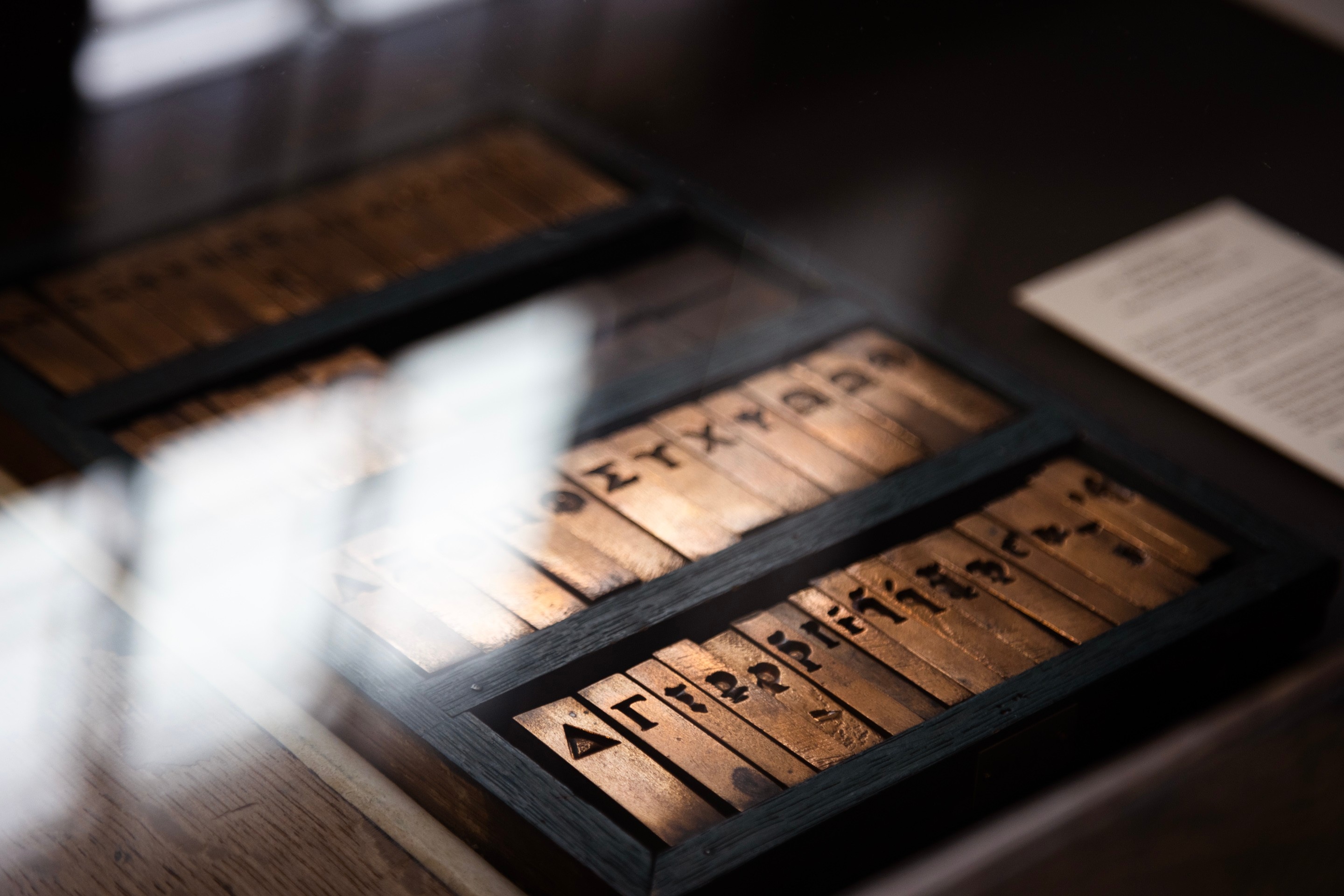 A case of special bronze Greek letter moveable type covered in glass reflecting the windows behind — Museum Plantin-Moretus, Antwerp, Belgium 