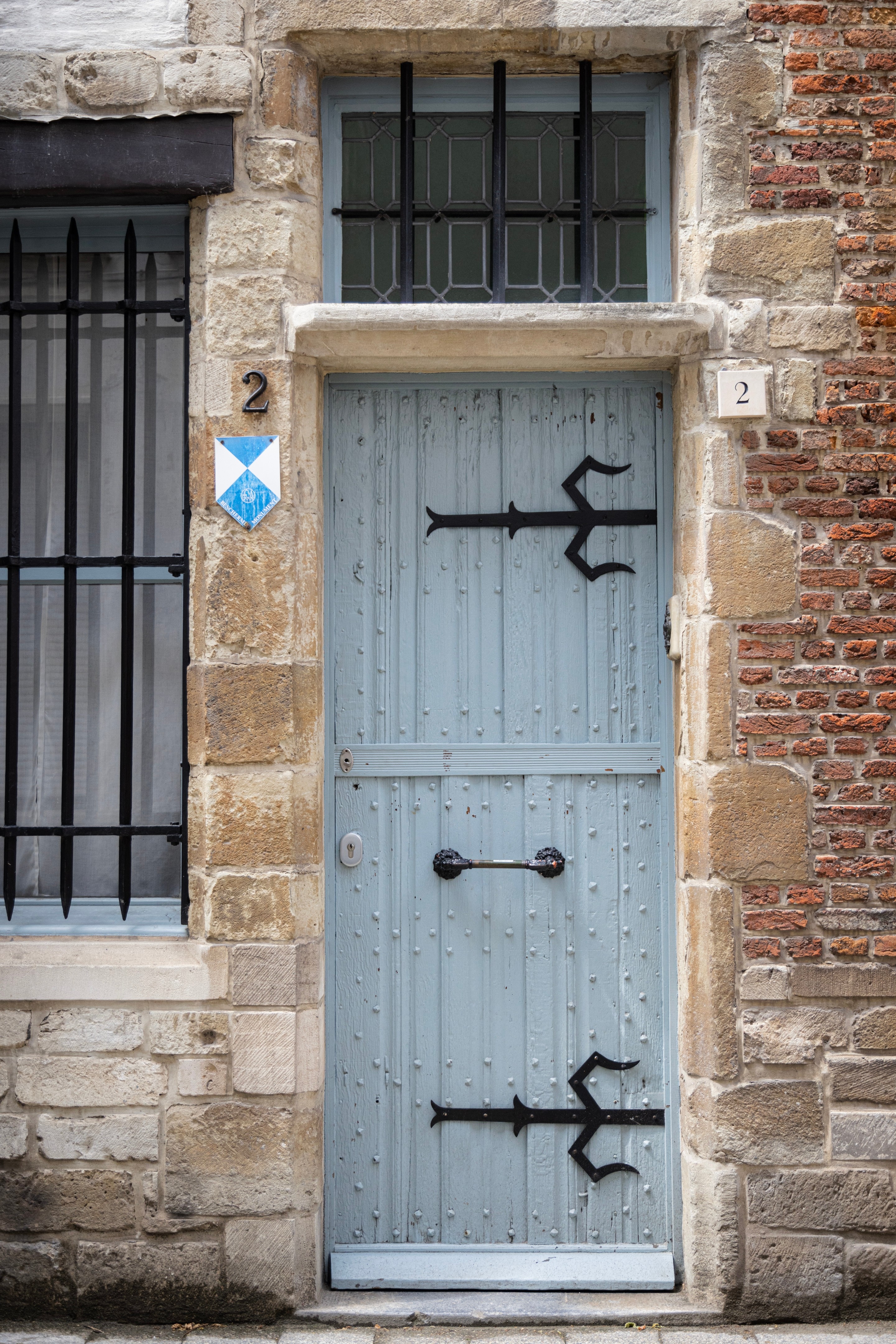 A very old pale blue door studded with iron bolts and decorated with large ornamental black iron hinges, fitted in a stone wall — Antwerp City, Belgium