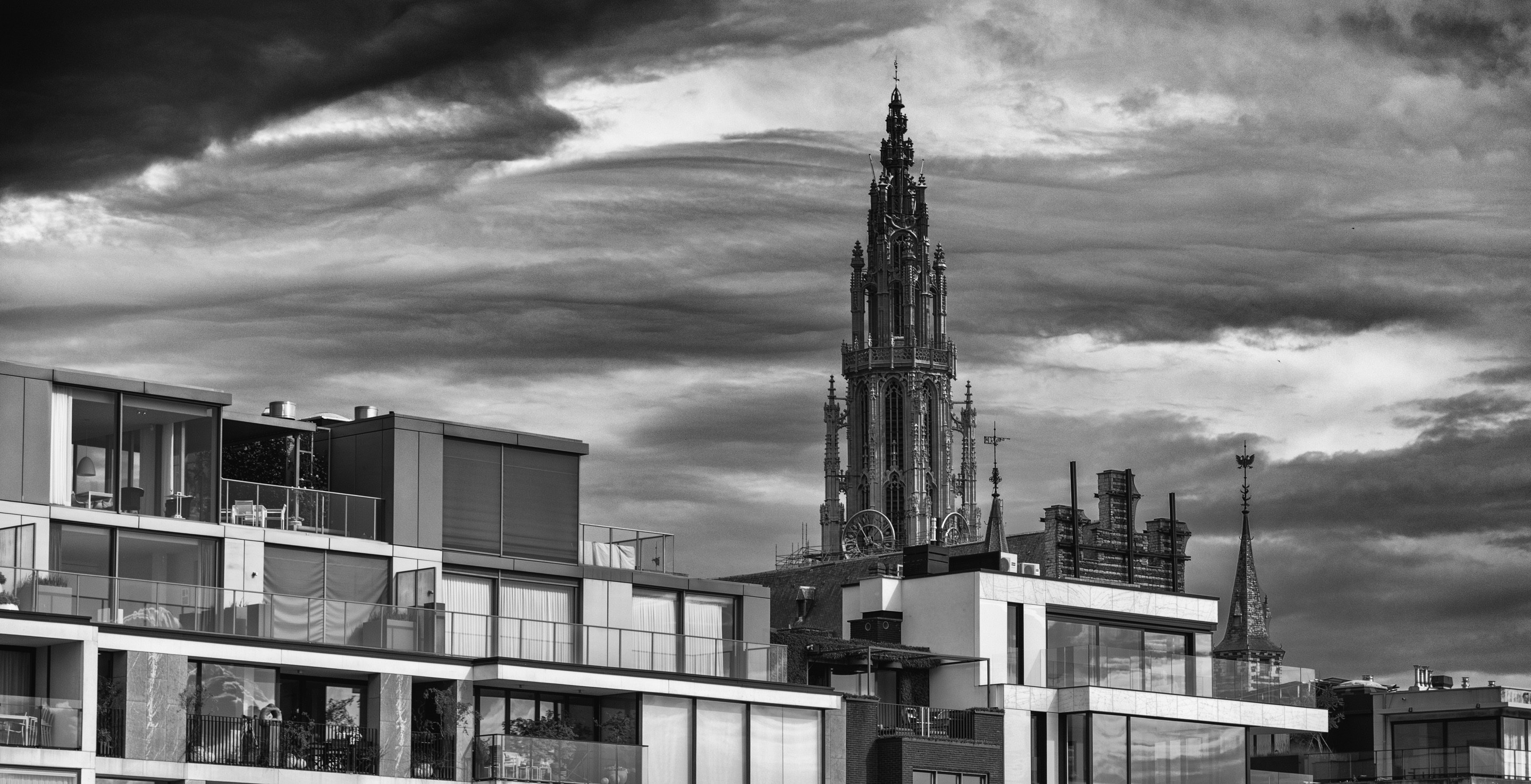 In the background the spire of the Cathedral of Our Lady rises behind some modern river-facing aparment buildings in the foreground — Het Steen, Antwerp City, Belgium