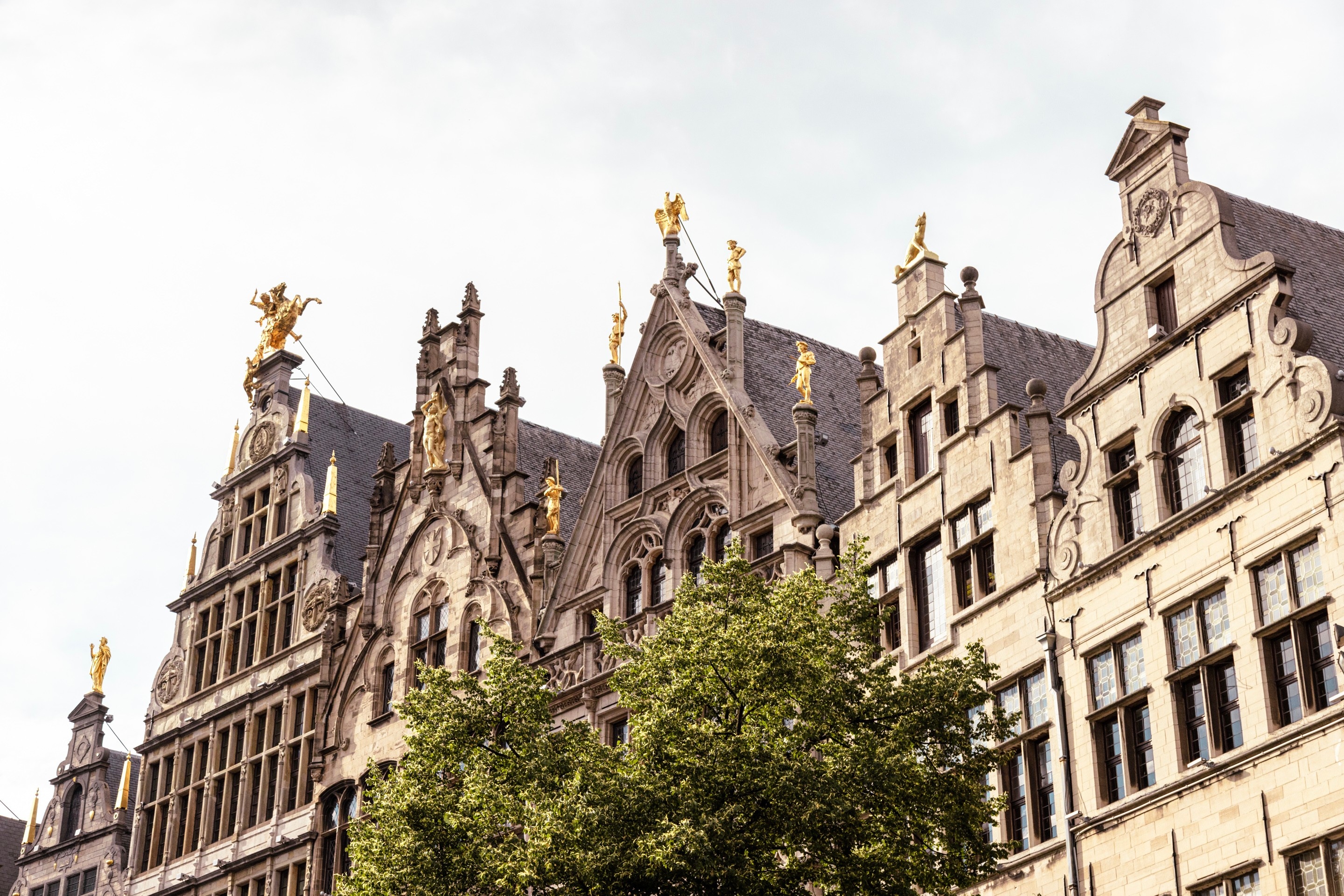 Five mediaeval mechant storefronts that surround the Market Square. It is decorated with golden statues; obelisks, priests and a large statue of St George slaying the dragon — Antwerp City, Belgium