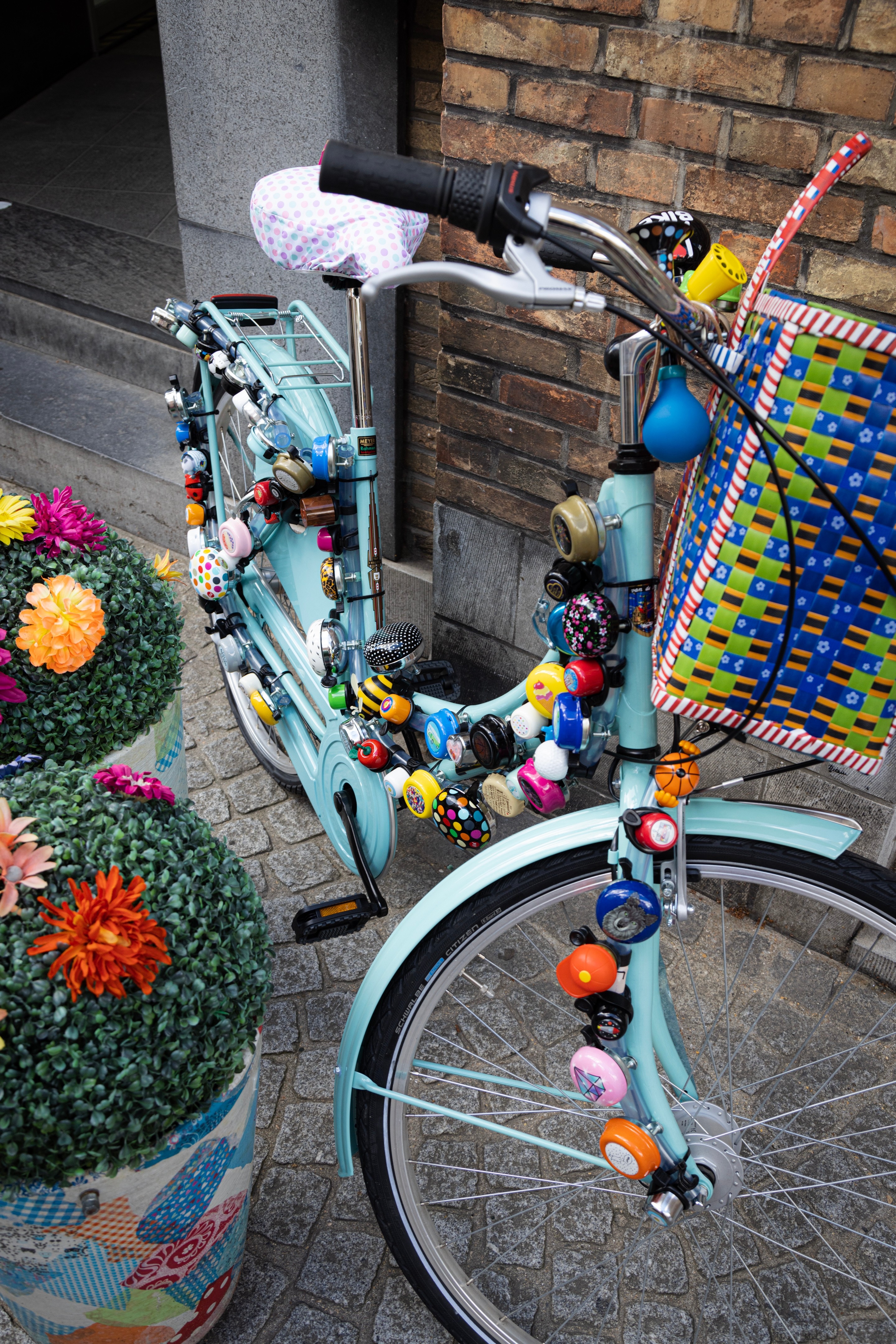A blue bicylcle covered in dozens of colourful bike bells leans agains a brick wall — Antwerp City, Belgium