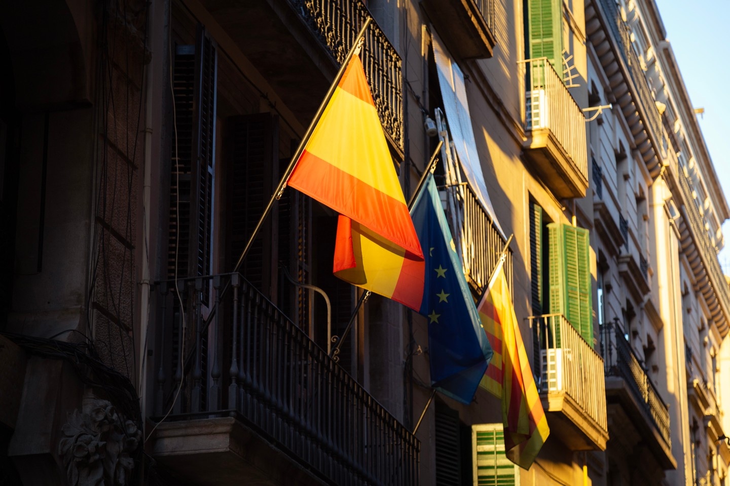 Spanish, European and Catalan flags hanging off a balcony in old Barcelona illuminated by a ray of evening sunshine.